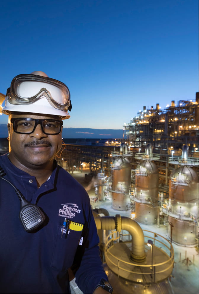 A man stands in the foreground with a chemical plant behind him